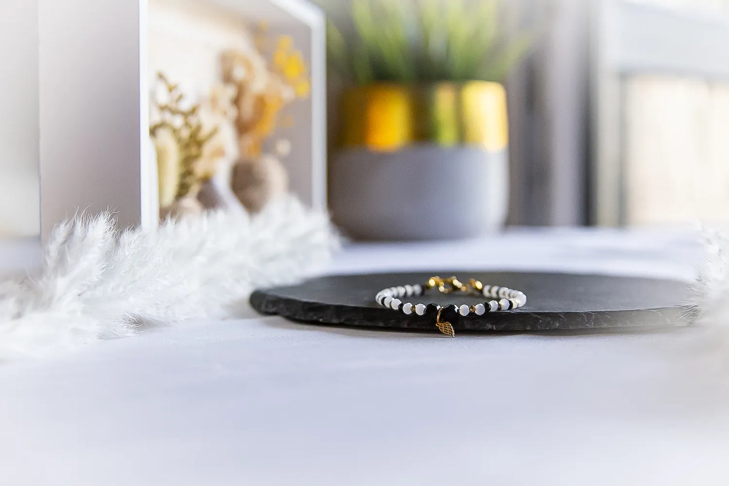 Anielskie Skrzydlo Bransoletka Z Turmalinu I Hematytu z delikatnym złotym anielskim skrzydłem, czarnymi turmalinami i białymi hematytami.