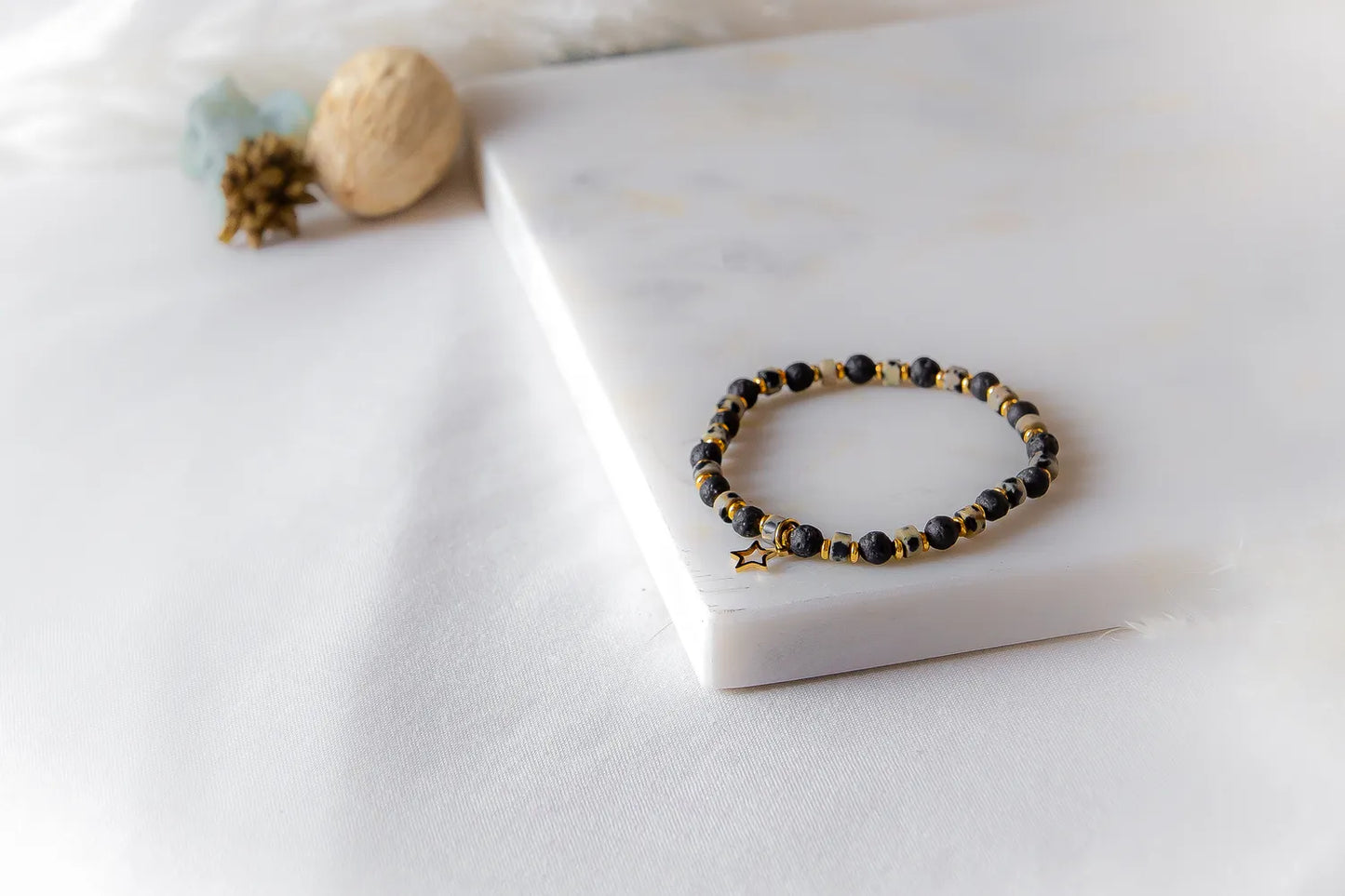 Gwiezdna Noc Bransoletka Czarne Kamienie z zawieszką gwiazdką, ułożONA NEATLY na marmurowej płytce, wśród subtelnych dekoracji.