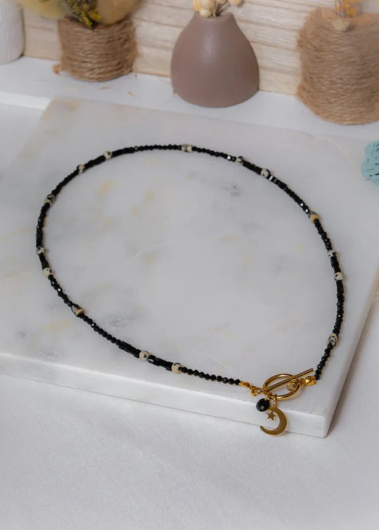 Księżycowy Talizman Naszyjnik Czarny Turmalin na białym tle, złoty zapięcie z uroczym księżycem i gwiazdą.