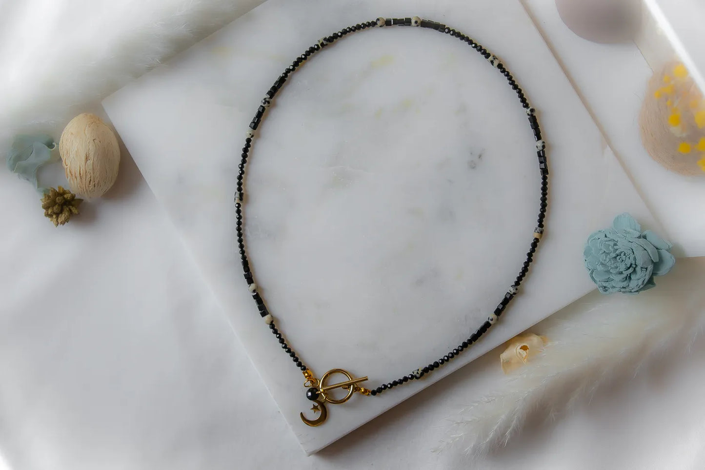 Księżycowy Talizman Naszyjnik Czarny Turmalin. Czarny, delikatny naszyjnik z czarnego turmalinu i białych kamieni, z ozdobnym zapięciem i złotym krzyżykiem.