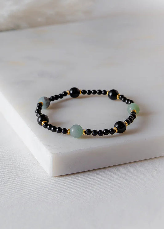 Lodowa Elegancja Bransoletka Agat Opal z czarnymi, zielonymi kamieniami i złotymi detalami na białej, marmurowej płytce.