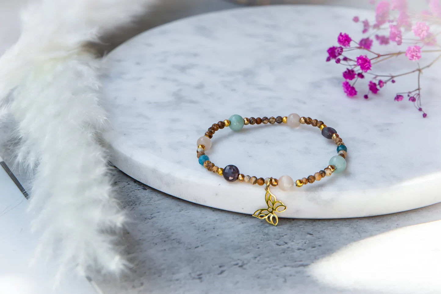 Motyli Taniec Bransoletka Z Kamieniami: złoty charms motyl na białej marmurowej desce.