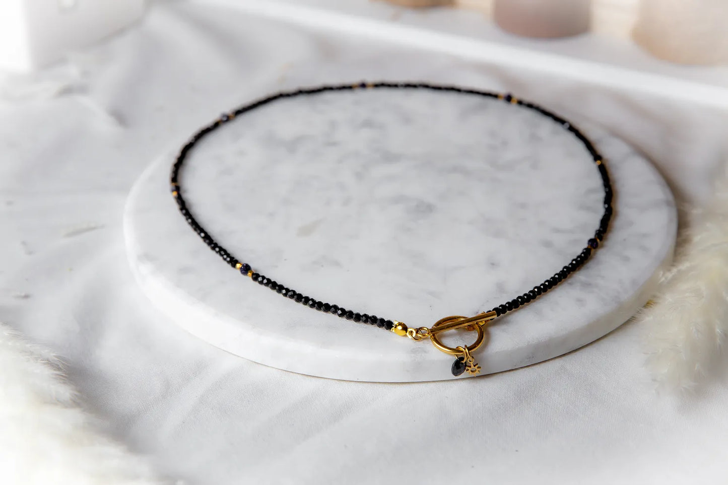 Noc Kairu Naszyjnik Czarny Koralik z złotym zapięciem toggle, ozdobiony drobnymi czarnymi fasetowanymi koralikami i złotymi akcentami.