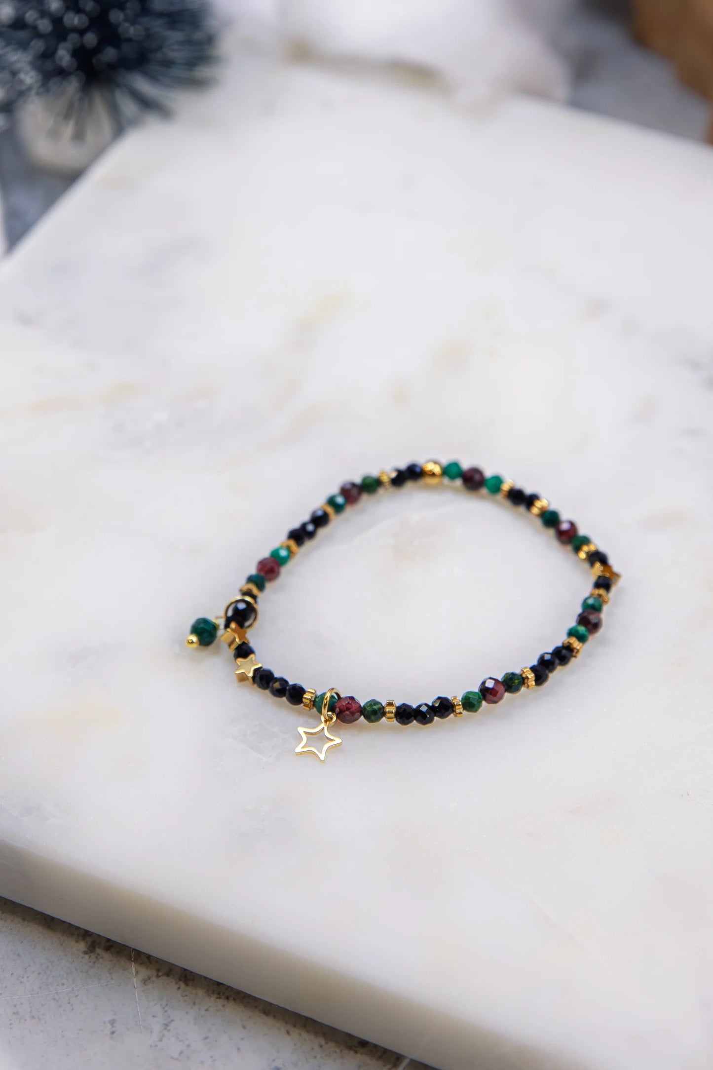 Widok z góry na elastyczną bransoletkę na gumce. Widoczny wzór ułożenia zielonych, czerwonych i czarnych kamieni przeplatanych drobnymi gwiazdkami z hematytu.