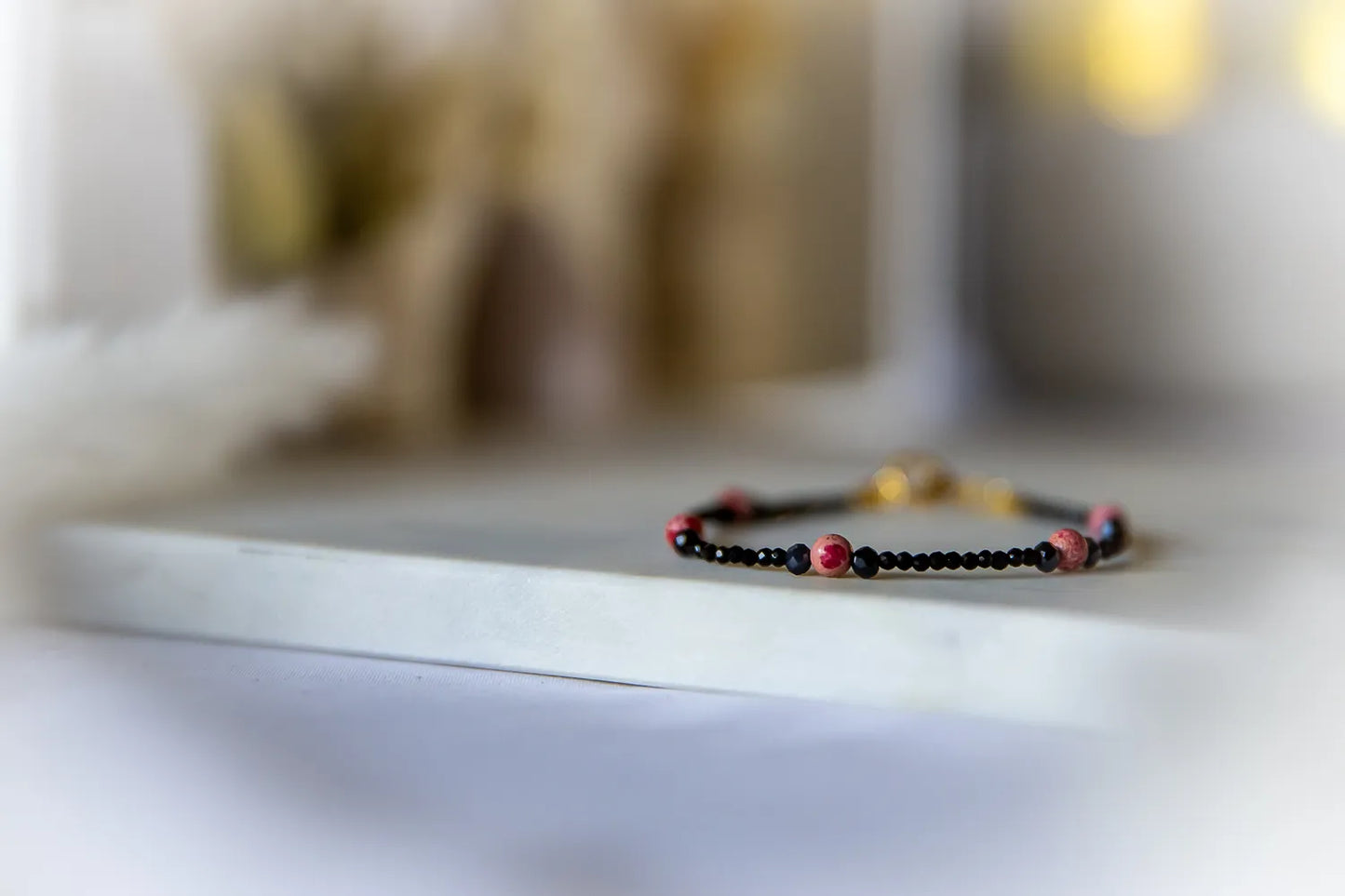 Różowa Ochrona Bransoletka Z Turmalinu I Jaspisu – subtelna, na białym tle, z różowymi kamieniami i czarnymi koralikami.