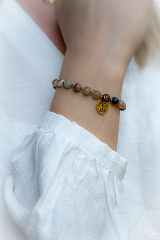 Bransoletka "Serce Rodziny" z agatów w odcieniach beżu i brązu, zdobiona złotym zawieszką-sercem, na ręce ubranej w białą bluzkę.