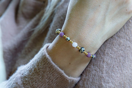 SŁODKI IMPULS - BRANSOLETKA Z JASPISU DALMATYŃSKIEGO I JADEITU. Bransoletka z kolorowymi kamieniami, w tym jaspisem dalmatyńskim i jadeitem, na tle delikatnej, beżowej bluzy. Ułożenie na nadgarstku.