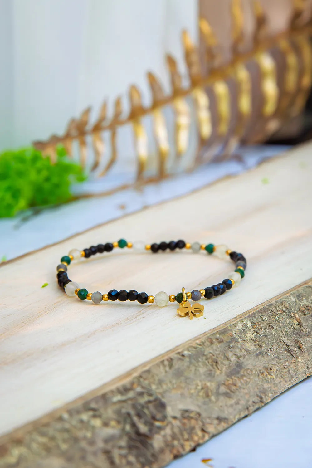SZEPT SZMARAGDOWEJ WYSPY - BRANSOLETKA Z LEPIDOLITU, CYTRYNU I LABRADORYTU. Kolorowa bransoletka z kamieni ze złotym symbolem szczęścia na drewnianej powierzchni.