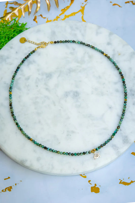 TARCZA ŻÓŁWIA - NASZYJNIK Z TURKUSU AFRYKAŃSKIEGO, naszyjnik z koralikami turkusowymi, zawieszka w kształcie żółwia, tło marmurowe, dekoracja z liści.