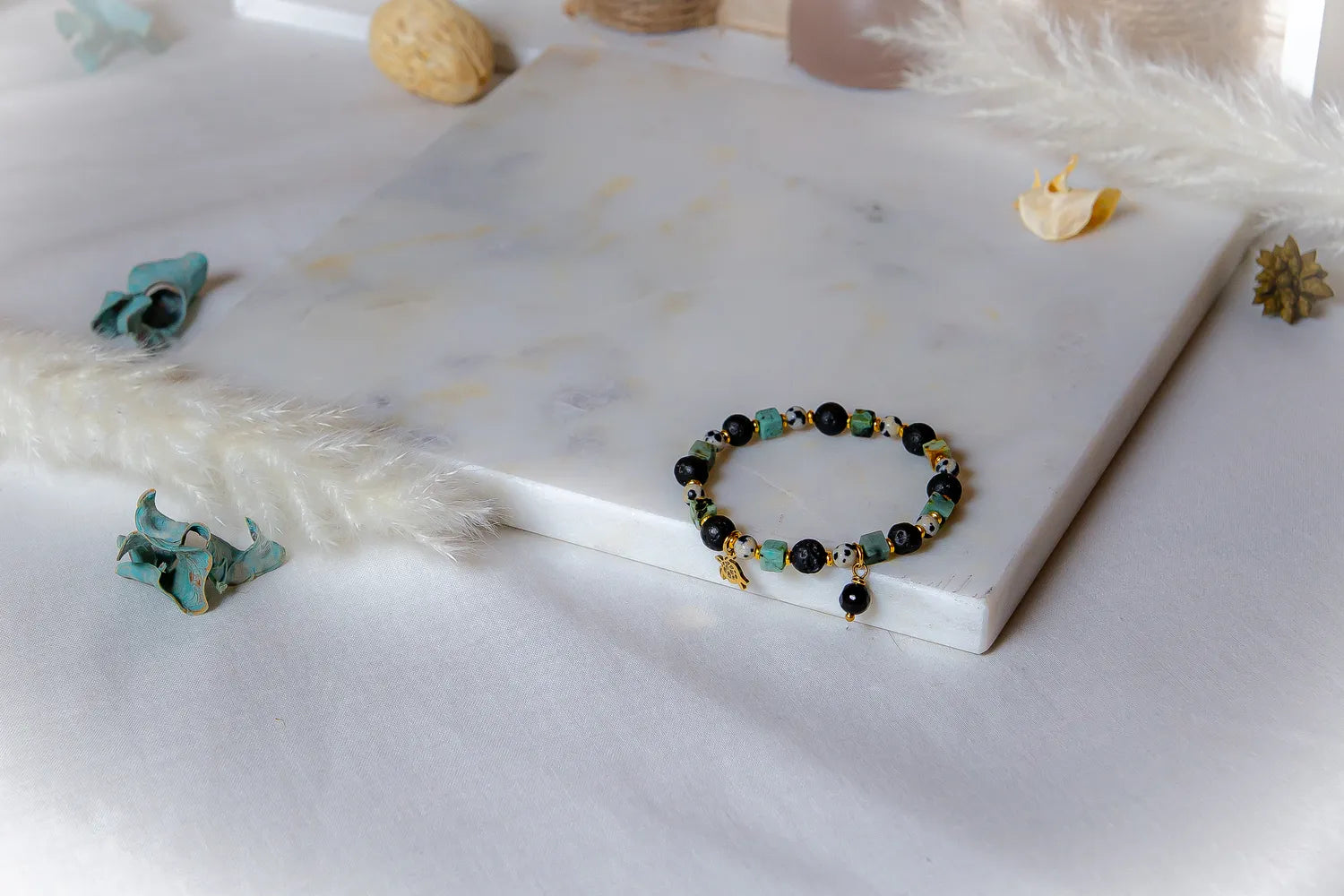 Afrykanska Harmonia Bransoletka Z Lawy Turkus z czarnymi i zielonymi kamieniami, z zawieszką, na białym tle z dekoracjami.