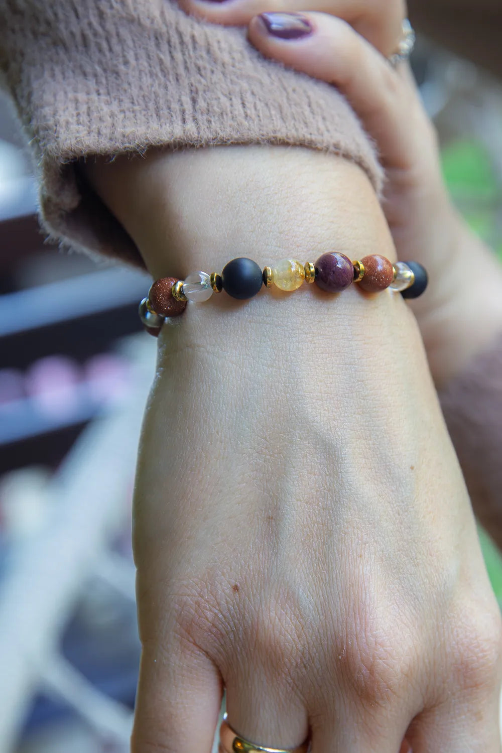 AMULET KRÓLOWEJ - BRANSOLETKA Z ONYKSU, CYTRYNU I JASPISU MORSKIEGO. Bransoletka z kolorowymi kamieniami na nadgarstku, tło zamazane, ułożenie naturalne.