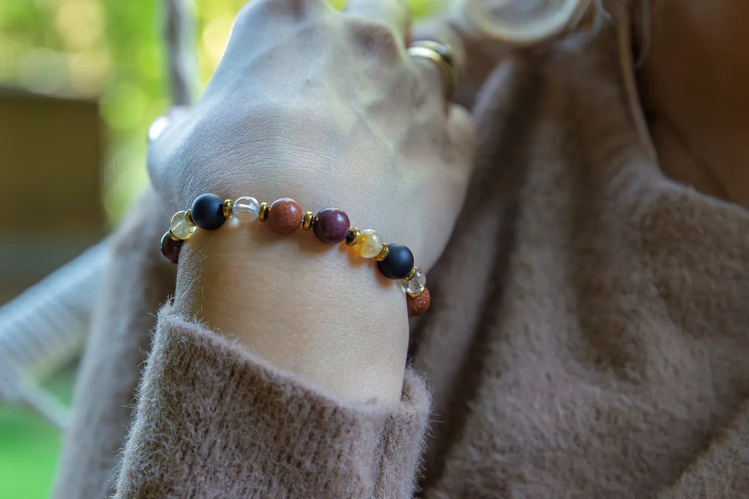 AMULET KRÓLOWEJ - BRANSOLETKA Z ONYKSU, CYTRYNU I JASPISU MORSKIEGO. Bransoletka z kolorowymi kamieniami, w tym czarnym onyksu, żółtym cytrynu i różowym jaspisu morskiego, na tle delikatnej, beżowej tkaniny.