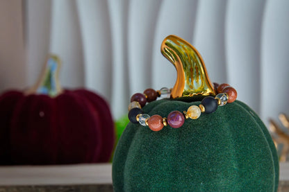 AMULET KRÓLOWEJ - BRANSOLETKA Z ONYKSU, CYTRYNU I JASPISU MORSKIEGO. Bransoletka z kolorowymi kamieniami naturalnymi, ułożona na zielonym aksamitnym podstawce w kształcie dyni, z pomarańczowym liściem w tle.