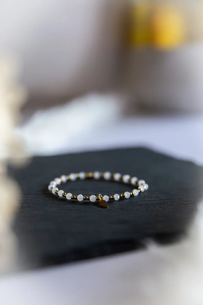 Anielski Blask Bransoletka Z Hematytu I Porcelany Elegancka na czarnym tle, z kamieniami białymi i złotymi detalami.