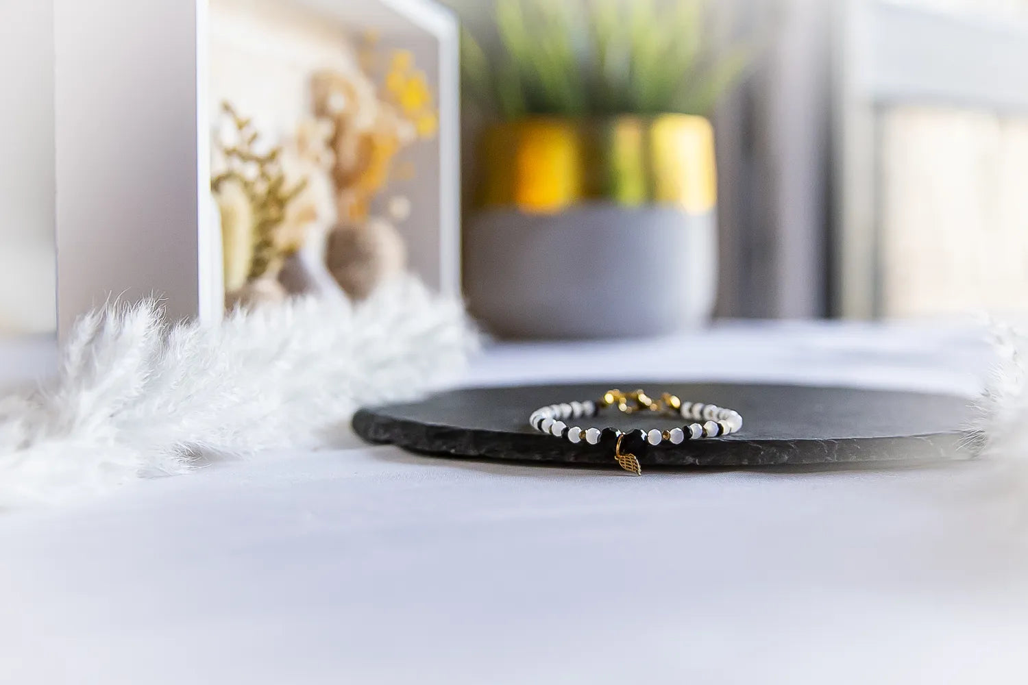 Anielskie Skrzydlo Bransoletka Z Turmalinu I Hematytu z delikatnym złotym anielskim skrzydłem, czarnymi turmalinami i białymi hematytami.