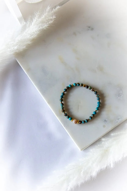 Błękitna Równowaga Bransoletka Agat Turkus z plecionymi kamieniami w odcieniach błękitu oraz złotymi przekładkami na marmurowej płytce.