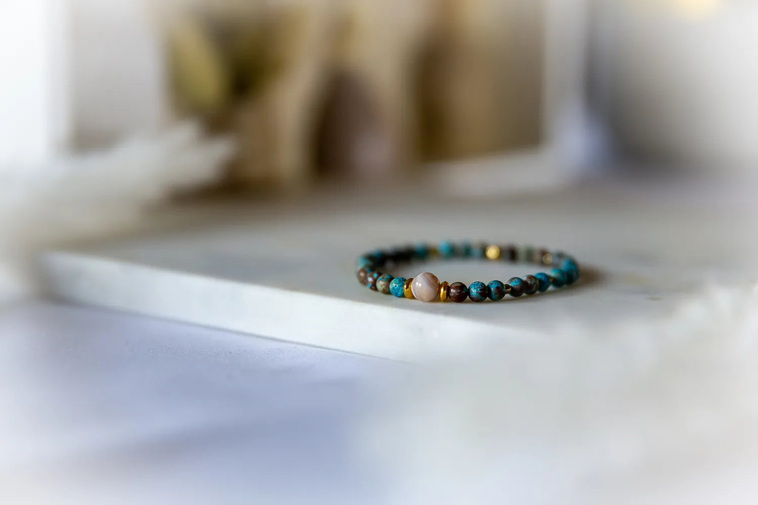 Blekitna Rownowaga Bransoletka Agat Turkus z beżowym centralnym kamieniem na marmurowej powierzchni, otoczona miękkim światłem.