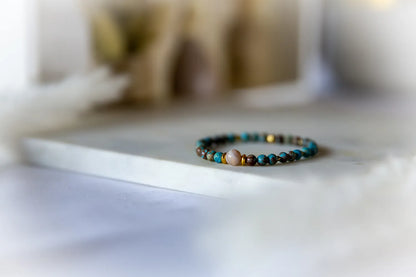 Blekitna Rownowaga Bransoletka Agat Turkus z beżowym centralnym kamieniem na marmurowej powierzchni, otoczona miękkim światłem.