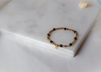 Cieple Serce Bransoletka Ziemia z lawowymi i beżowymi kamieniami oraz złotym serduszkiem, na tle białego marmuru.