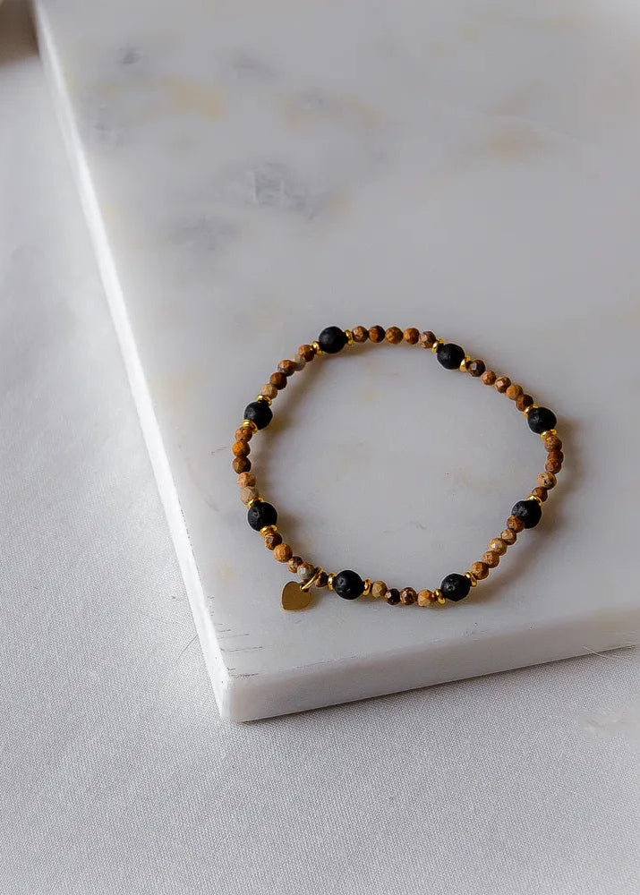 Cieple Serce Bransoletka Ziemia z brązowymi i czarnymi kamieniami oraz złotym sercem, ułożona na białym marmurze.