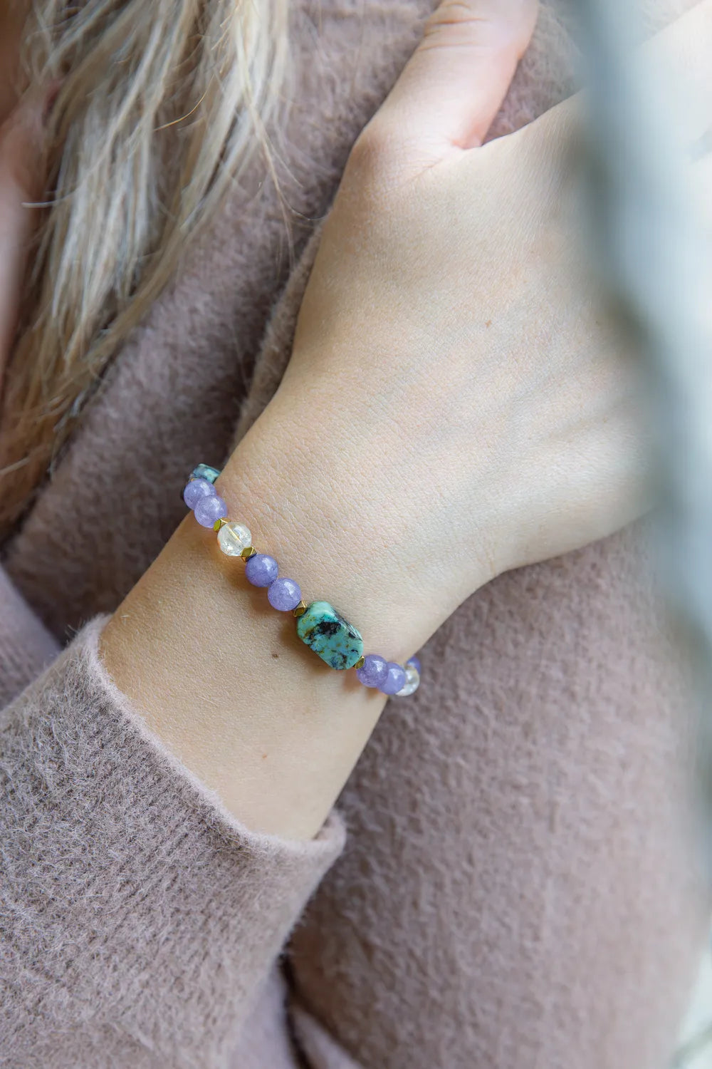 Bransoletka 'DROGA DUSZY' z turkusem afrykańskim, ametystem i cytrynem, widoczna na nadgarstku kobiety. Kamienie ułożone w szereg na delikatnym tle.