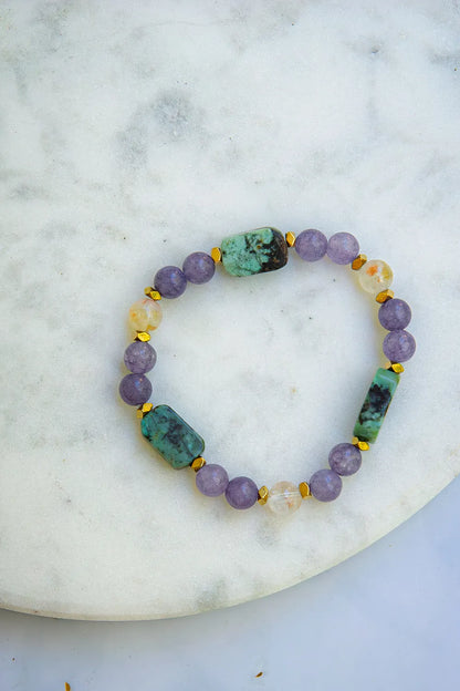 DROGA DUSZY - BRANSOLETKA Z TURKUSU AFRYKAŃSKIEGO, AMETYSTU I CYTRYNU. Bransoletka z kolorowymi kamieniami, w tym turkus afrykański, ametyst i cytryn, ułożona na białym marmurowym tle.