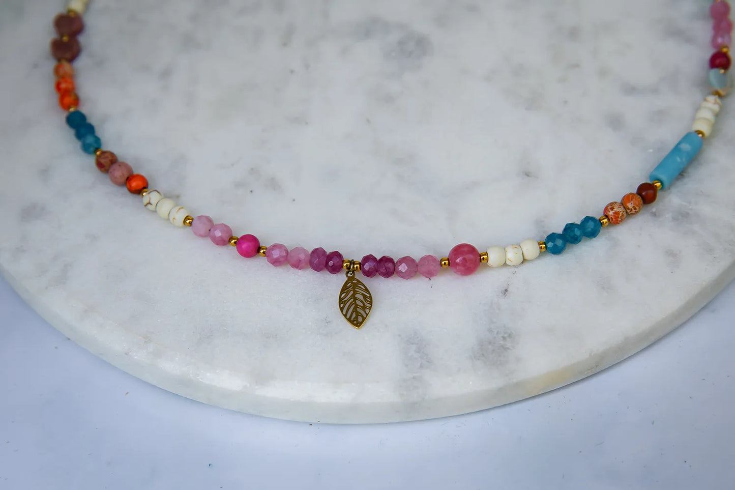 FESTIWAL RADOŚCI - NASZYJNIK Z JADEITU TURMALINOWEGO, TURMALINU I JASPISU. Naszyjnik z kolorowymi koralikami jadeitu turmalinowego, turmalinu i jaspisu, ułożony na marmurowym tle z dodatkiem złotego liścia.