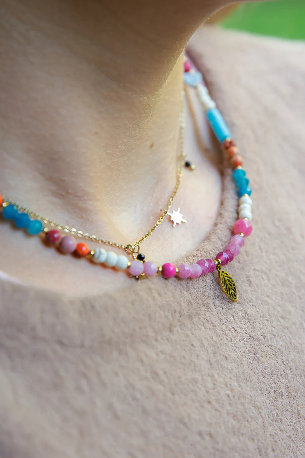 FESTIWAL RADOŚCI - NASZYJNIK Z JADEITU TURMALINOWEGO, TURMALINU I JASPISU. Naszyjnik z kolorowymi kamieniami, w tym turmalinowym jadeitem, turmalinem i jaspisem, na szyi modelki. Tło z beżowej tkaniny.