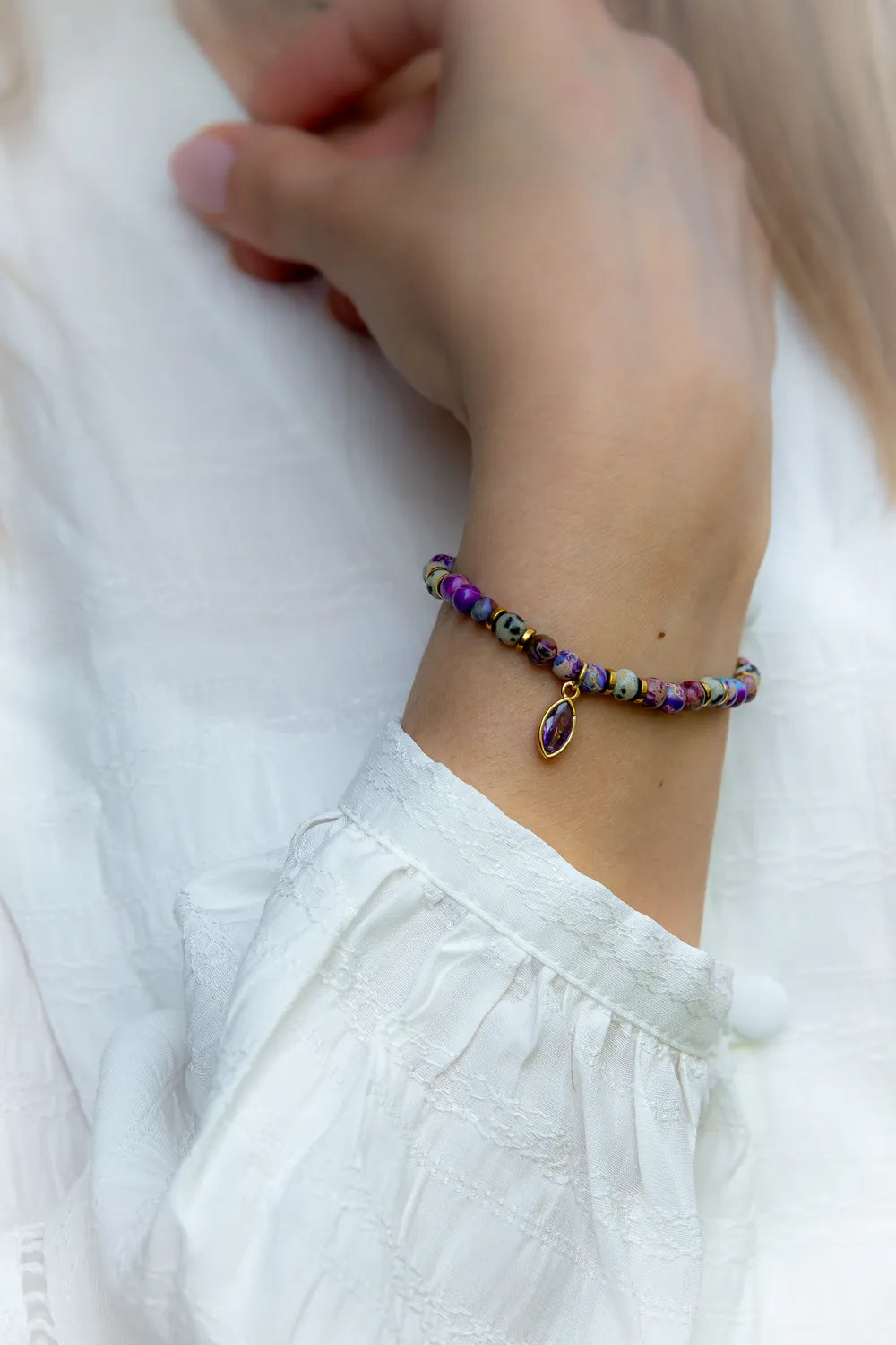 Fioletowa Zorza Bransoletka Z Jaspisu Kolorowe Koraliki z wiszącym medalionem z kwarcowego fioletowego kamienia, na białej bluzce.