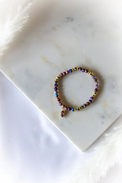 Fioletowa Zorza Bransoletka Z Jaspisu Marmur z dominującymi fioletami i niebieskościami na białym marmurze, ozdobiona złotymi elementami i fasetowanym fioletowym kamieniem.