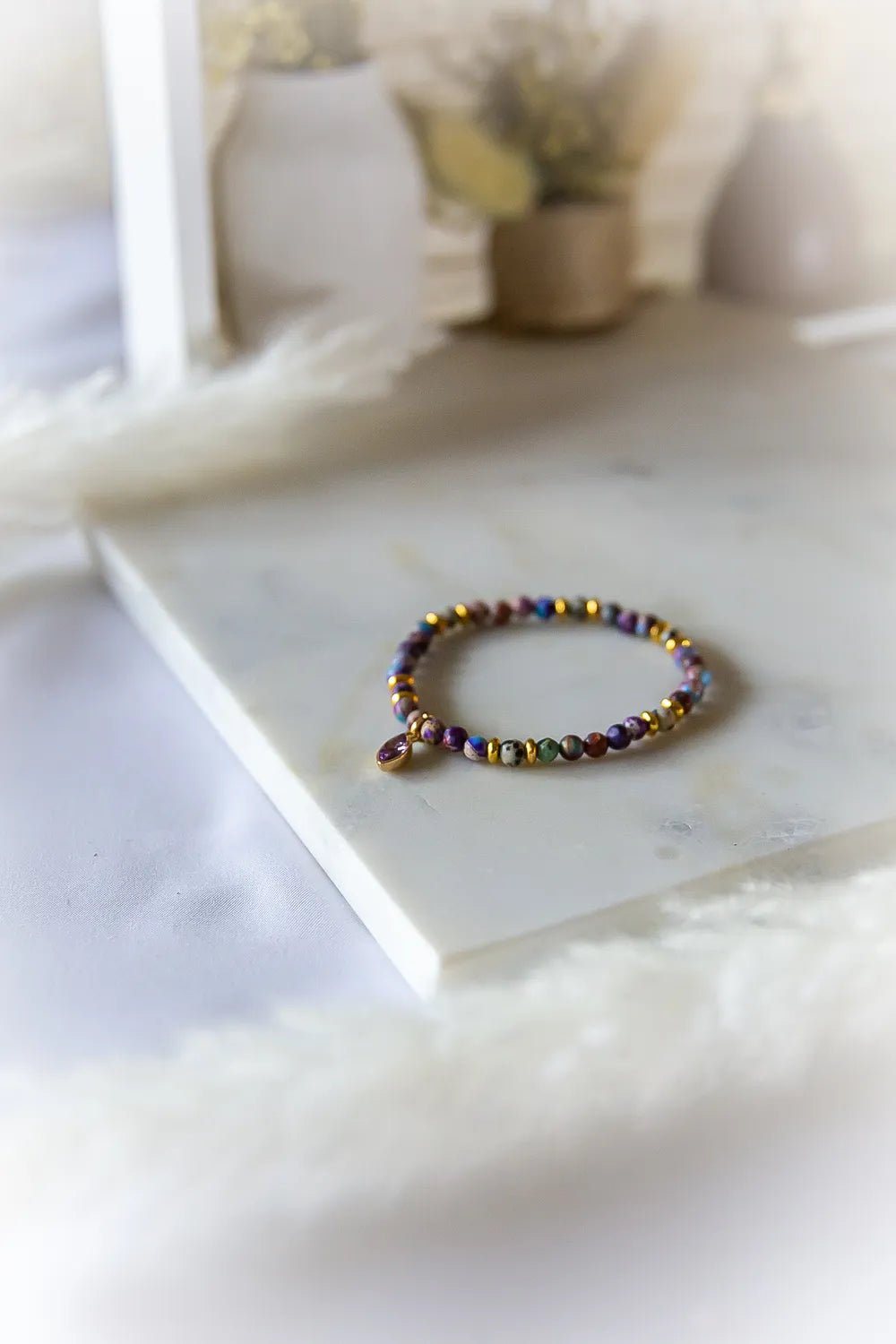 Fioletowa Zorza Bransoletka Z Jaspisu Marmur z wielobarwnymi kamieniami i złotymi przekładkami, leżąca na białym marmurze.