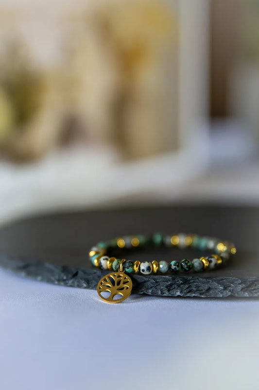 Gaj Madrosci Bransoletka Turkus Jaspis z zawieszką drzewko, kamienie turkusowe i jaspisowe o nieregularnych kształtach, na ciemnym tle.