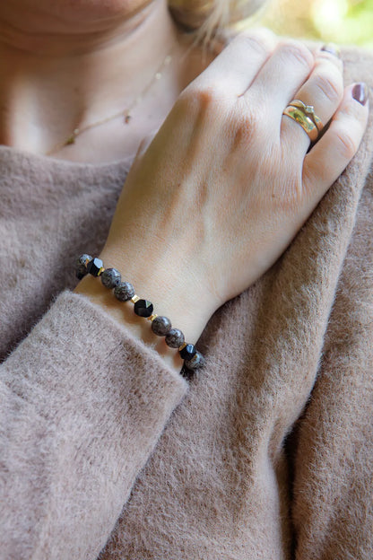 GŁĘBOKIE KORZENIE - BRANSOLETKA Z BRĄZOWEGO OBSYDIANU I ONYKSU na nadgarstku, z widocznymi brązowymi i czarnymi kamieniami, na tle beżowego swetra.