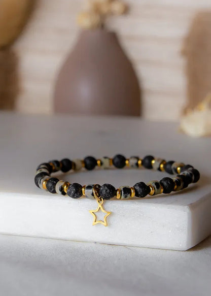 Gwiezdna Noc Bransoletka: czarna lawa, jaspis dalmatyński, złota gwiazdka. Na białym tle w otoczeniu ozdób.