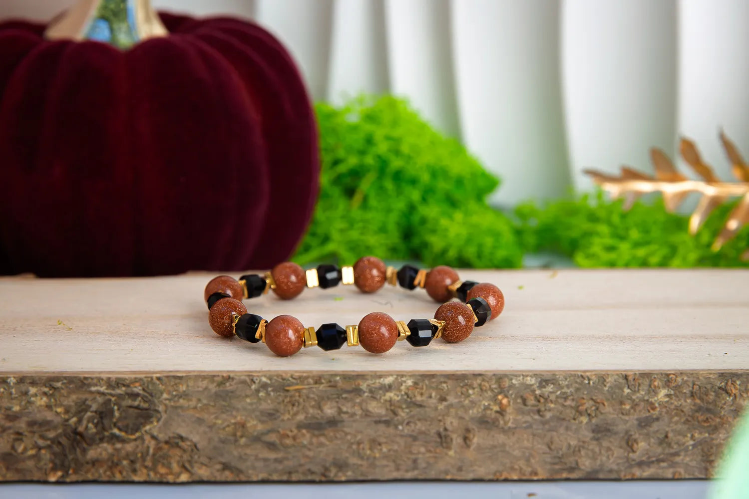 GWIEZDNA PUSTYNIA - BRANSOLETKA Z PIASKU PUSTYNI I CZARNEGO AGATU. Bransoletka z koralikami z piasku pustyni i czarnego agatu, ułożona na drewnianym bloku z zielonym tłem i dekoracją.