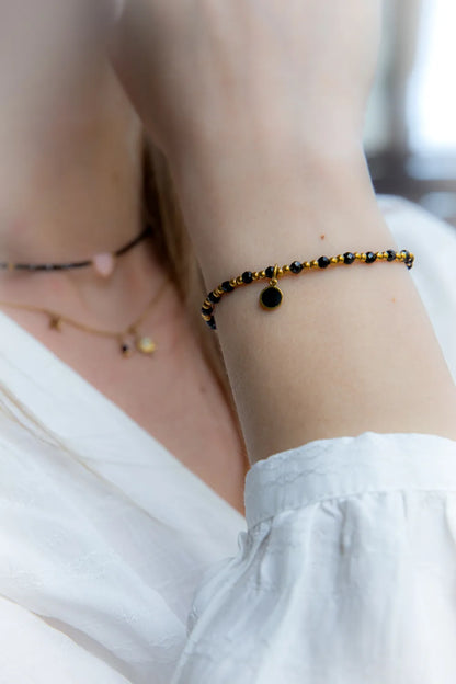 Klasyczna Elegancja Bransoletka Z Hematytu I Czarnego Turmalinu z złotym elementem na nadgarstku, w tle subtelne naszyjniki.