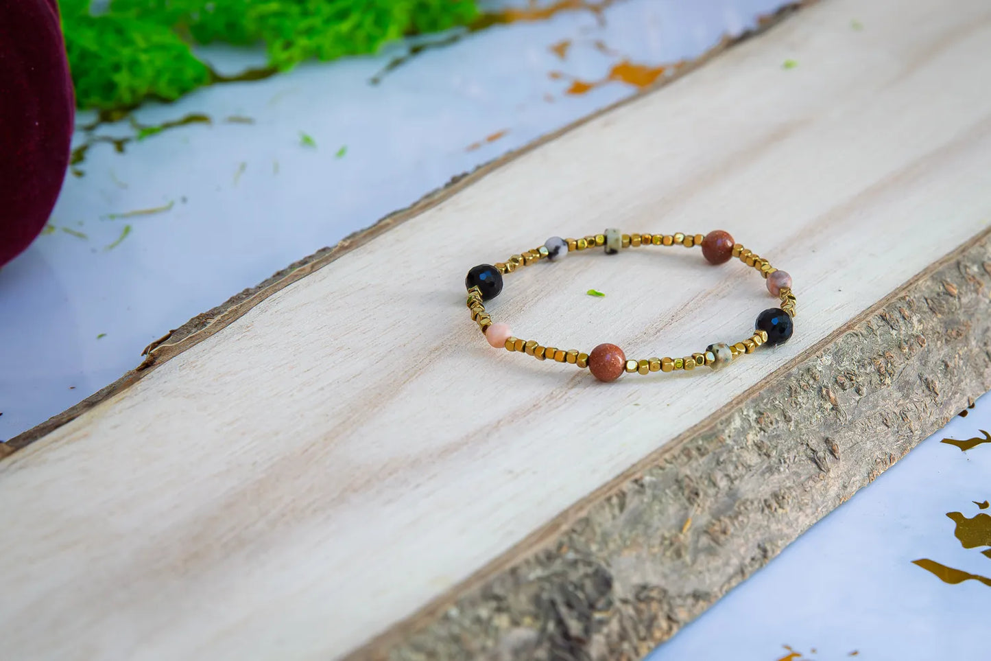 KOMPAS DUSZY - BRANSOLETKA Z TURMALINU, RODONITU I PIASKU PUSTYNI. Bransoletka z kolorowymi koralikami turmalinu, rodonitu i piasku pustyni, ułożona na drewnianym tle.