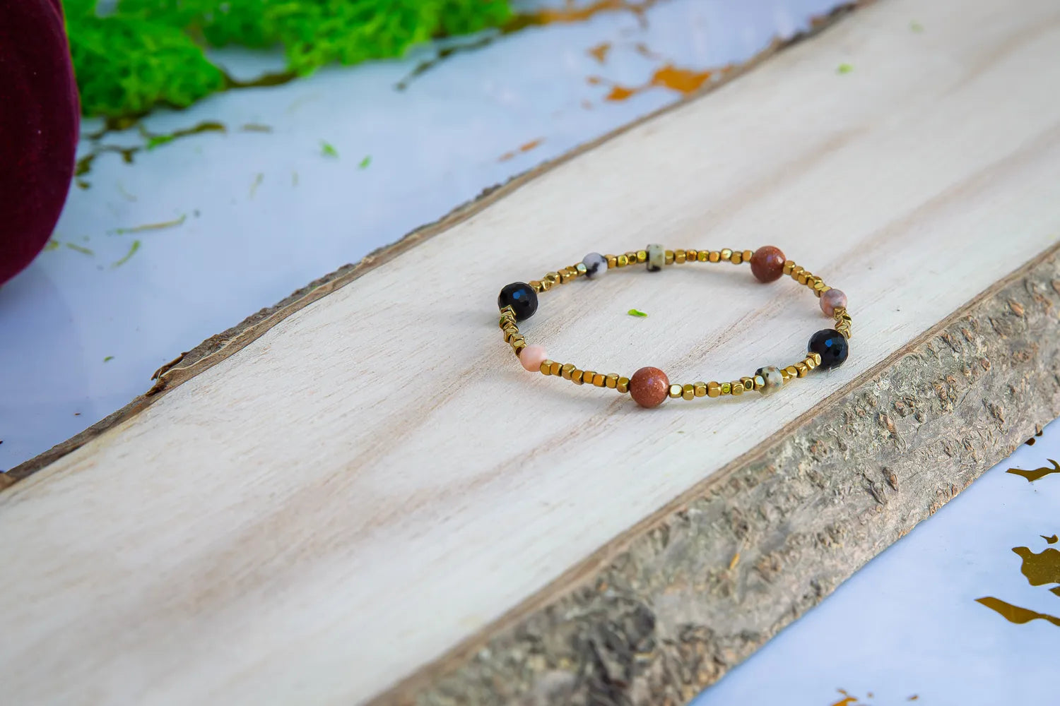 KOMPAS DUSZY - BRANSOLETKA Z TURMALINU, RODONITU I PIASKU PUSTYNI. Bransoletka z kolorowymi koralikami turmalinu, rodonitu i piasku pustyni, ułożona na drewnianym tle.