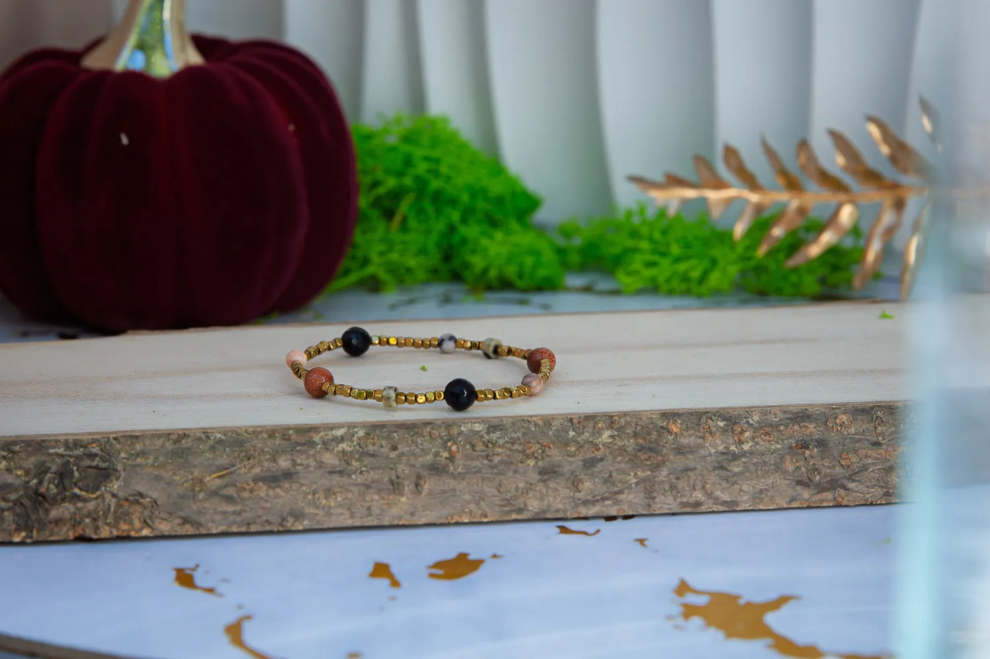 KOMPAS DUSZY - BRANSOLETKA Z TURMALINU, RODONITU I PIASKU PUSTYNI. Bransoletka z kolorowymi koralikami na drewnianym tle, zielone mech i czerwona dynia w tle.
