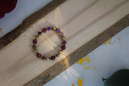 KRÓLEWSKA INTUICJA - BRANSOLETKA Z JASPISU CESARSKIEGO I FIOLETOWEGO AGATU, złożona z fioletowych i czarno-białych kamieni, leżąca na drewnianym tle z delikatnymi cieniami.