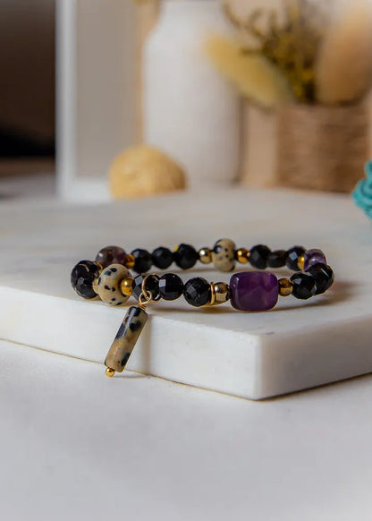 Królewska Ochrona Bransoletka Z Turmalinem I Ametystem: wielokolorowa bransoletka z czarnymi i fioletowymi kamieniami, na marmurowej powierzchni.