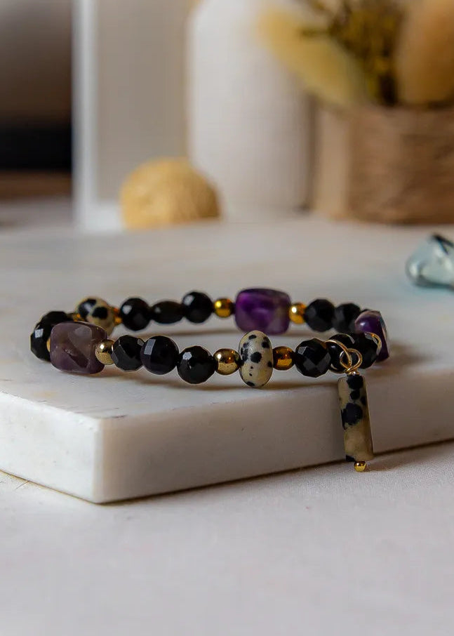 Królewska Ochrona Bransoletka Z Turmalinu I Ametystu Elegancka Biżuteria – zbliżenie na bransoletkę z czarnymi, fioletowymi i białymi kamieniami na białej powierzchni.