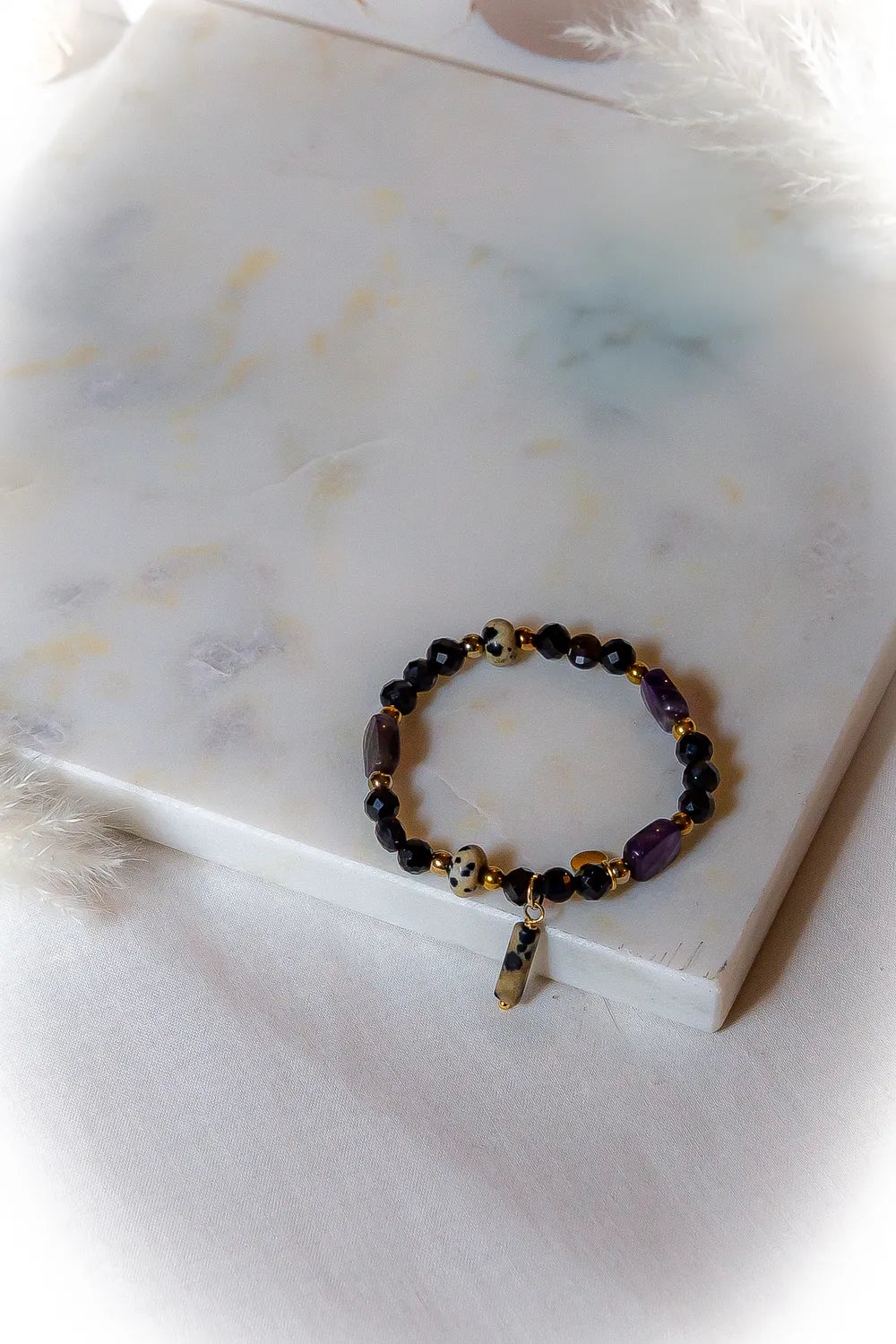 Królewska Ochrona Bransoletka Z Turmalinu I Ametystu Elegancka Biżuteria z białymi drobinkami na kamieniach na marmurowej powierzchni.