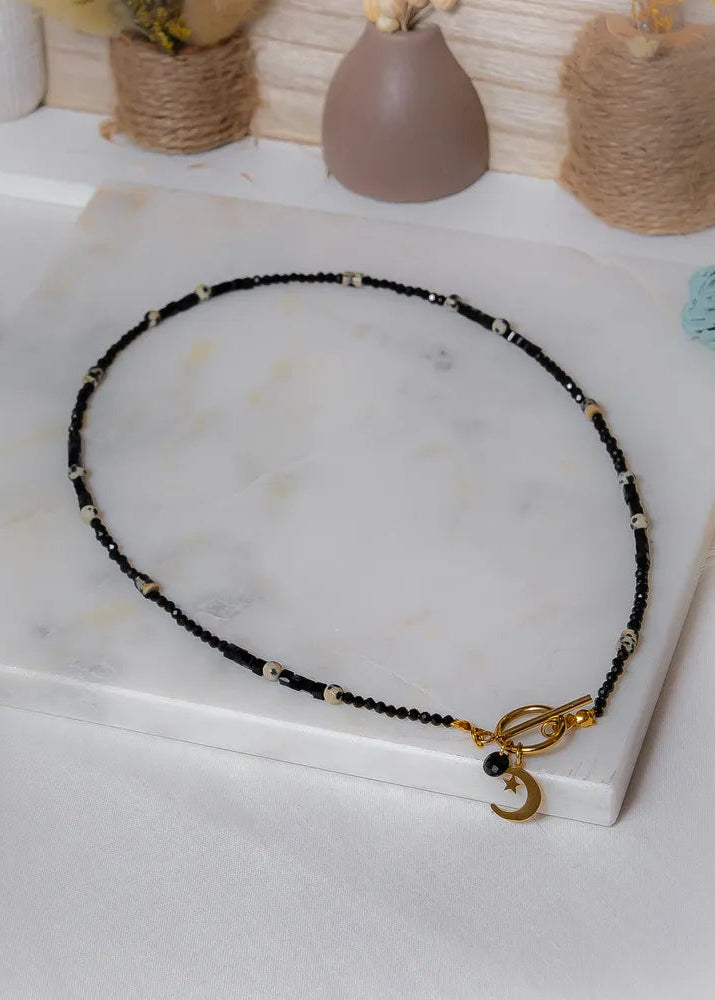 Księżycowy Talizman Naszyjnik Czarny Turmalin na białym tle, złoty zapięcie z uroczym księżycem i gwiazdą.