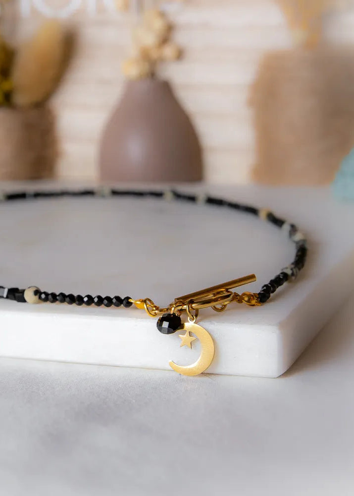 Księżycowy Talizman Naszyjnik Czarny Turmalin: złoty księżyc z gwiazdką i czarnym turmalinem na naszyjniku z czarnych i kamiennych koralików, ozdobiony zapięciem toggle.
