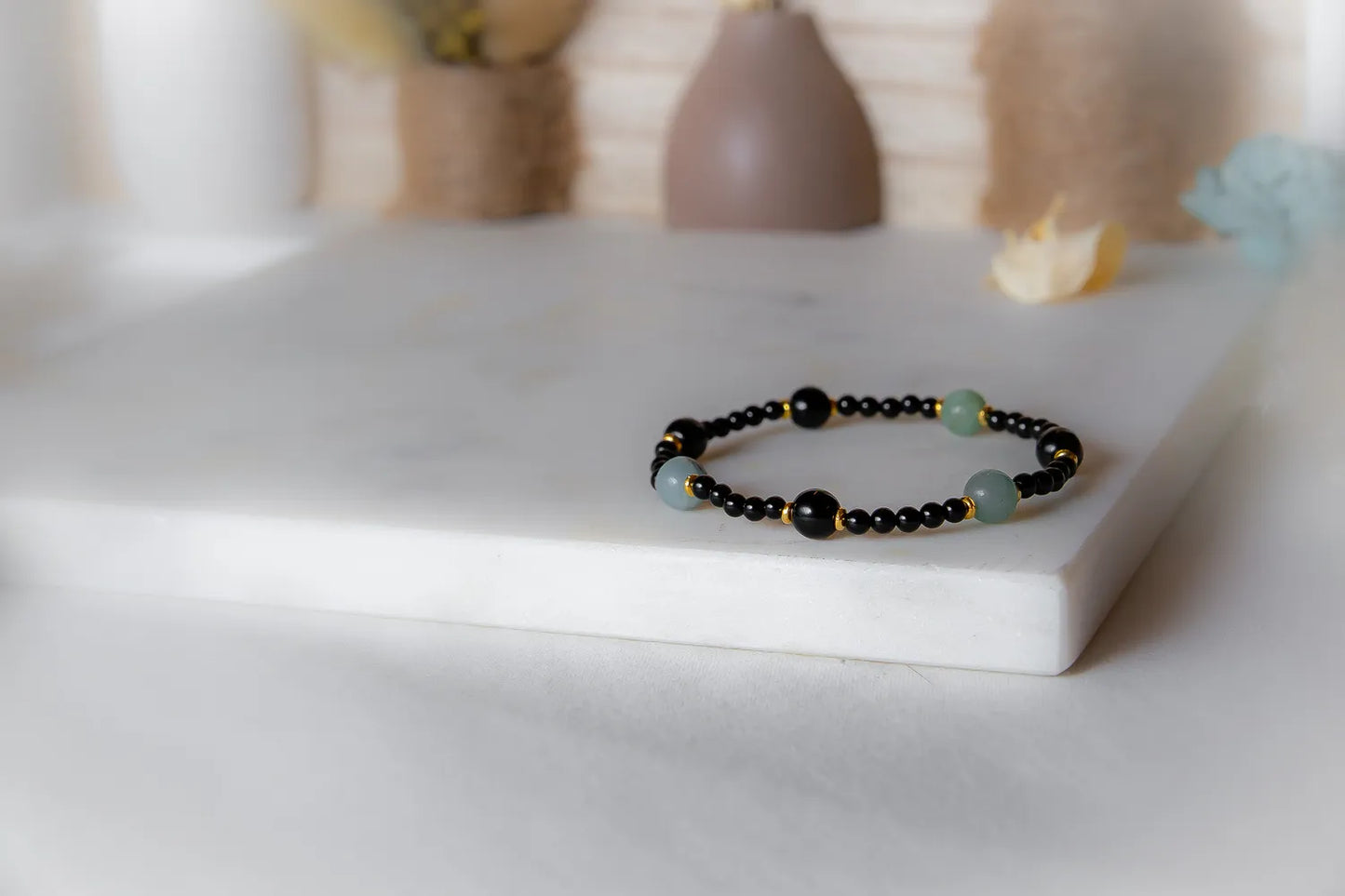 Lodowa Elegancja Bransoletka Agat Opal: czarny sznur z czarnymi, zielonymi i złotymi koralikami na skale.