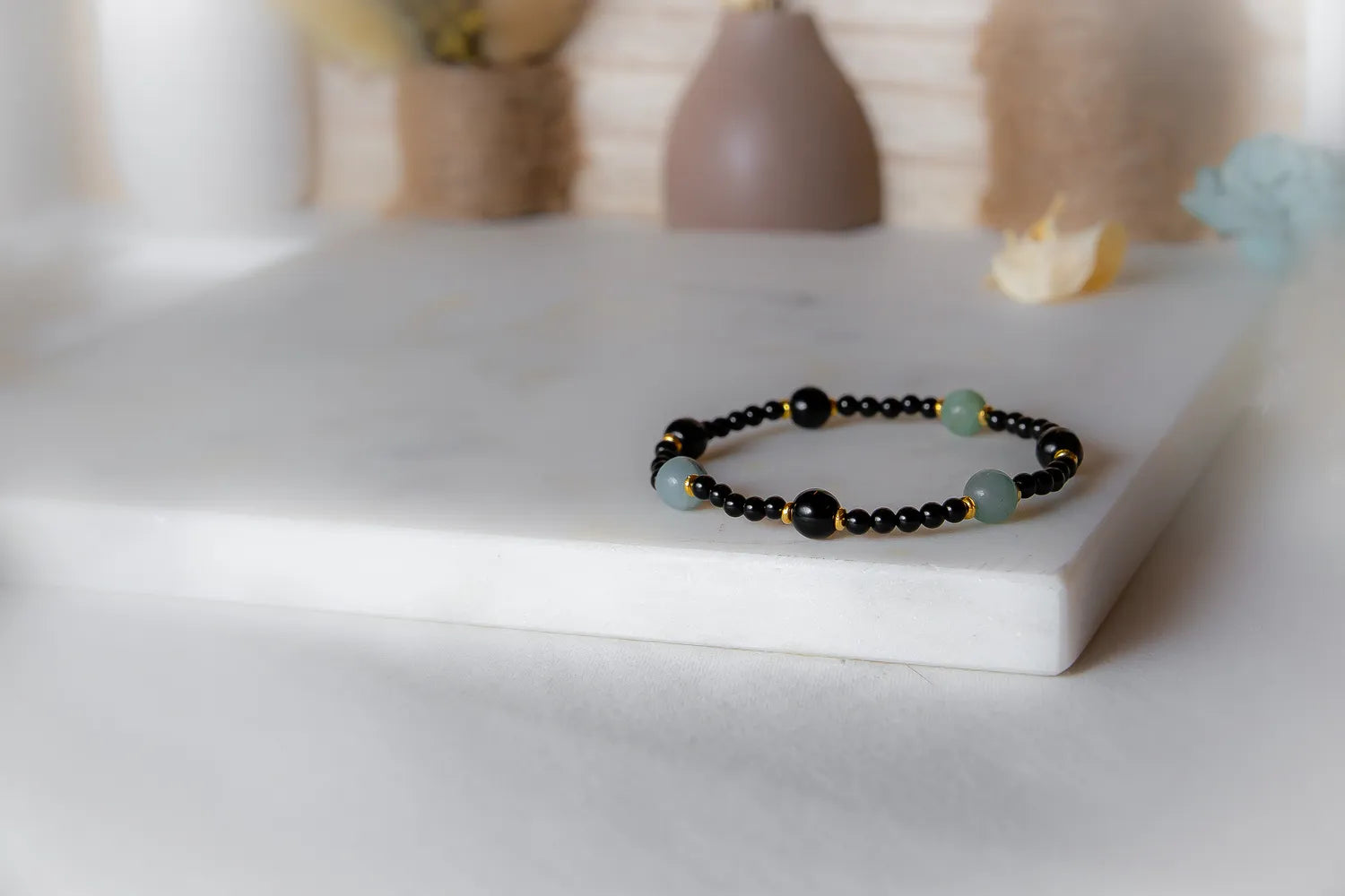 Lodowa Elegancja Bransoletka Agat Opal: czarny sznur z czarnymi, zielonymi i złotymi koralikami na skale.