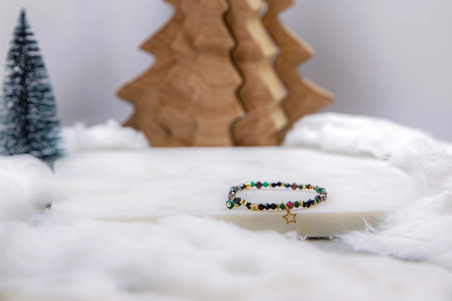 Bransoletka z motywem gwiazdy jako magiczny talizman-drogowskaz na prezent świąteczny. Biżuteria z kamieni naturalnych w otoczeniu choinek i sztucznego śniegu.