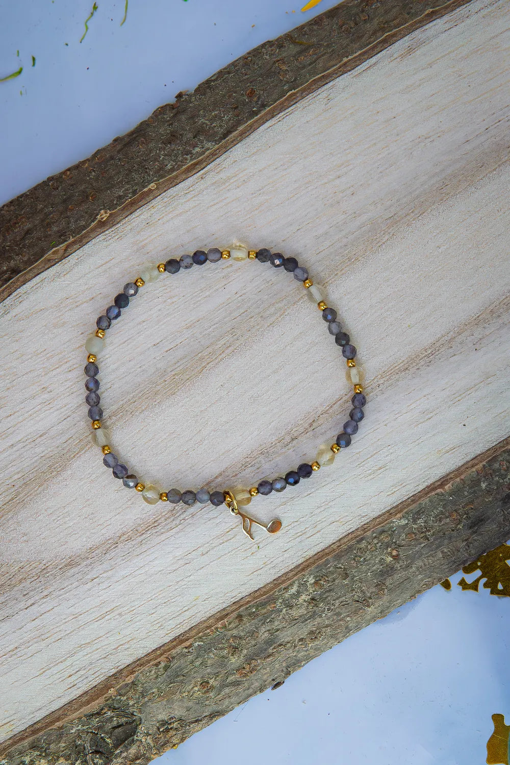 MELODIA MAGII - BRANSOLETKA Z LABRADORYTU I CYTRYNU, bransoletka z koralikami labradorytu i cytrynu, ułożona na drewnianym tle, z dodatkowym złotym elementem.