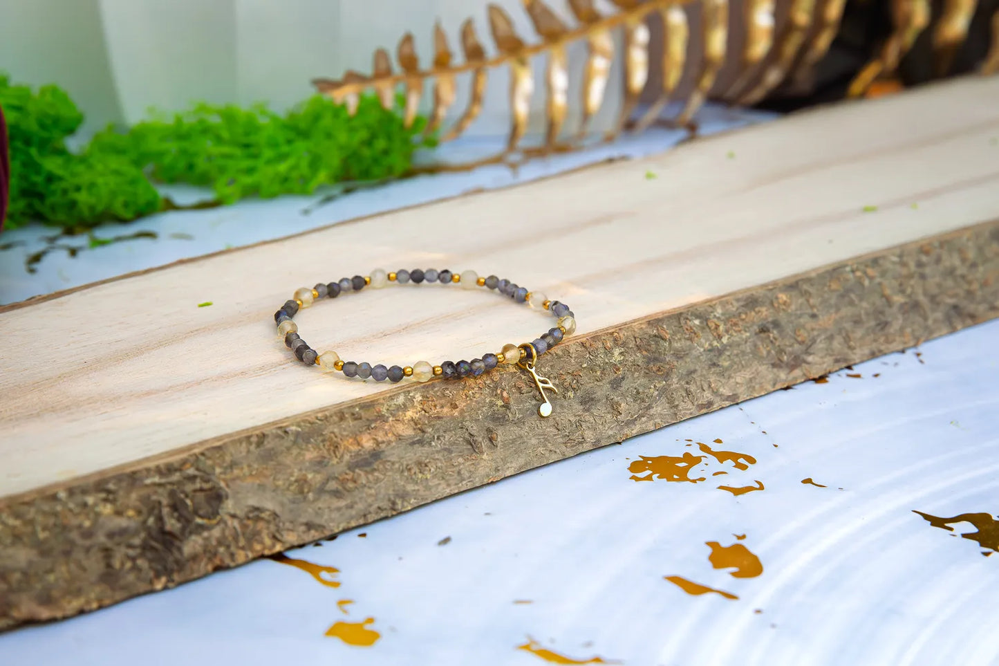 MELODIA MAGII - BRANSOLETKA Z LABRADORYTU I CYTRYNU, bransoletka z koralikami labradorytu i cytrynu, ułożona na drewnianym pomoście z zielonym mchem i złotymi liśćmi w tle.